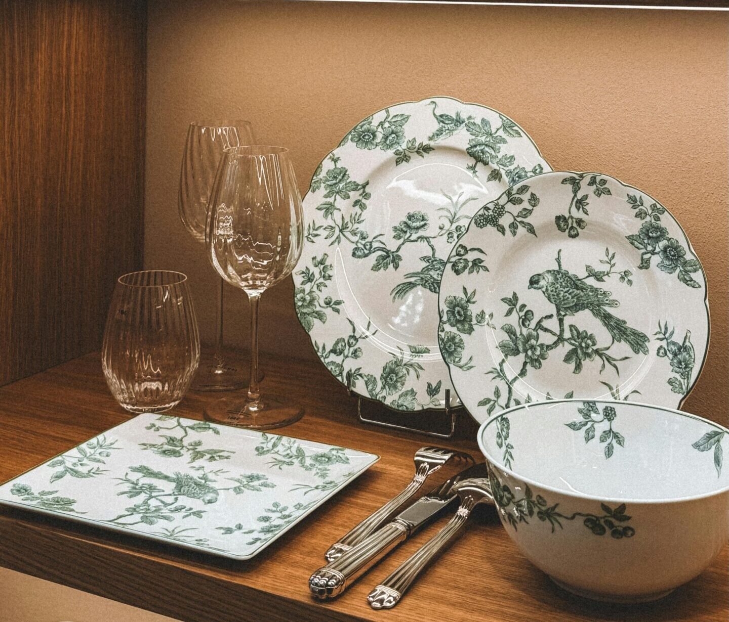 A stylish arrangement of floral porcelain, glassware, and teapots on modern wooden shelves.