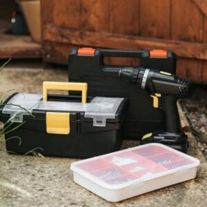 Electric screwdriver with black case placed near entrance of garage with boxes of instruments on sidewalk with grass on street