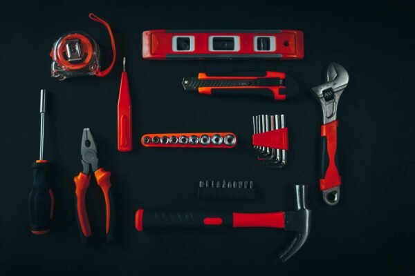 Top view arrangement of various repair tools including pliers hammer screwdriver and tape measure placed on black table