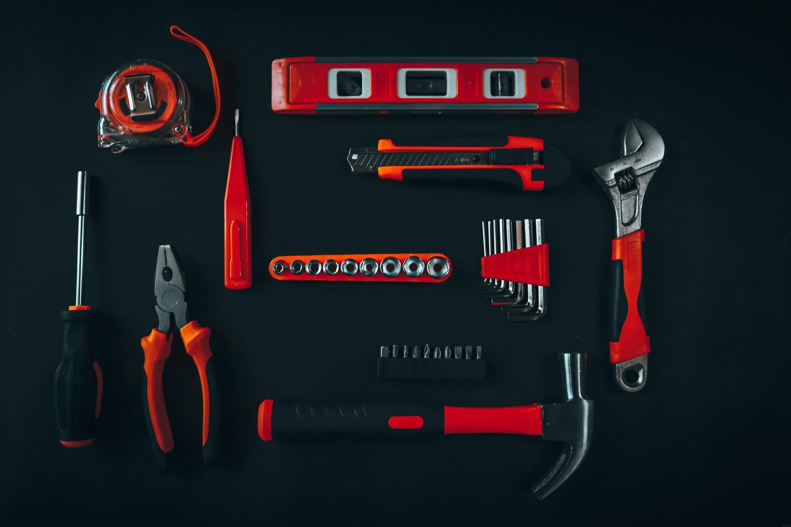 Top view arrangement of various repair tools including pliers hammer screwdriver and tape measure placed on black table