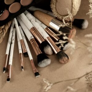 From above of makeup brushes with eyeshadows on beige background with branches of dried plants